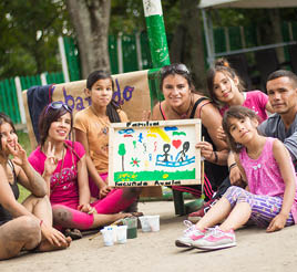 A group of youth sit on the ground in a park and show off a canvas painting.