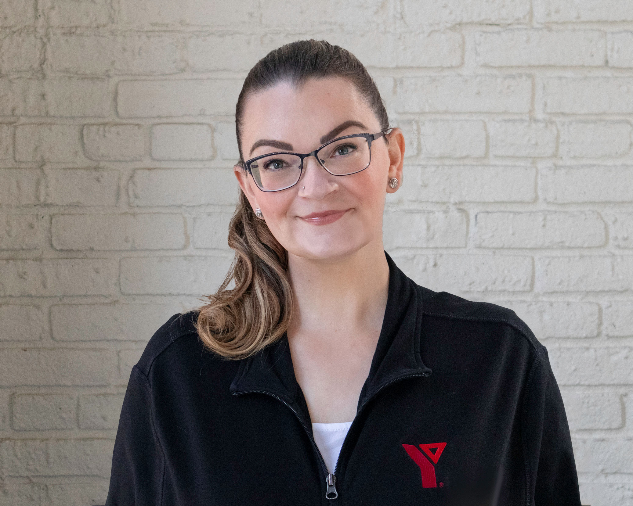 LauraSvajlenko_YMCAHeadshot_Websize A young, professional woman, Laura Svajlenko, wearing glasses and a YMCA uniform smiles.
