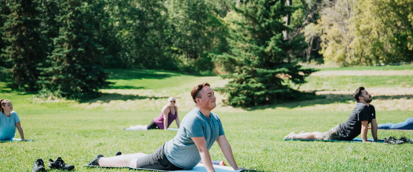A diverse group of young adults participate in a yoga class outdoors.
