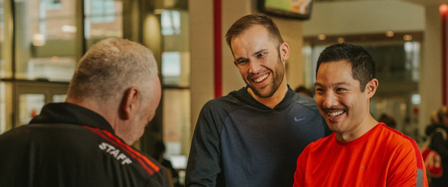 Two men standing at a YMCA front desk, talking to a YMCA staff member.