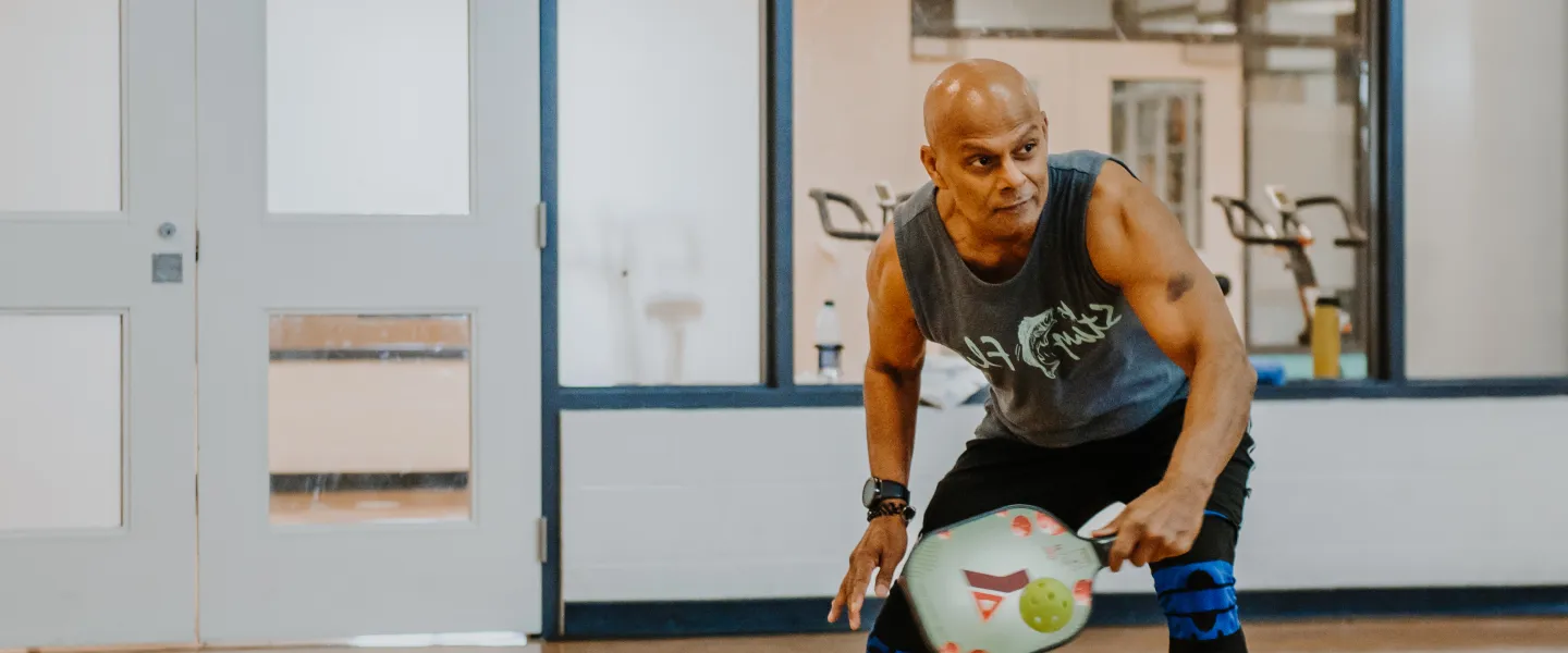 A man winds up for a swing while playing pickleball in a gymnasium.