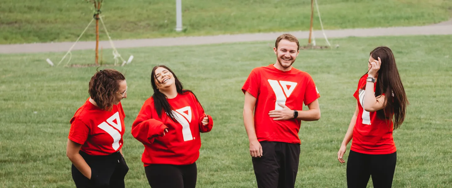 A group of YMCA day camp staff laugh together outdoors.