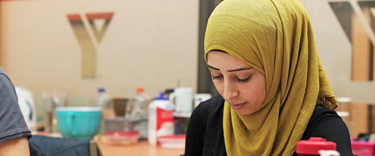 A woman wearing a hijab sits at a table and writes notes during a workshop.