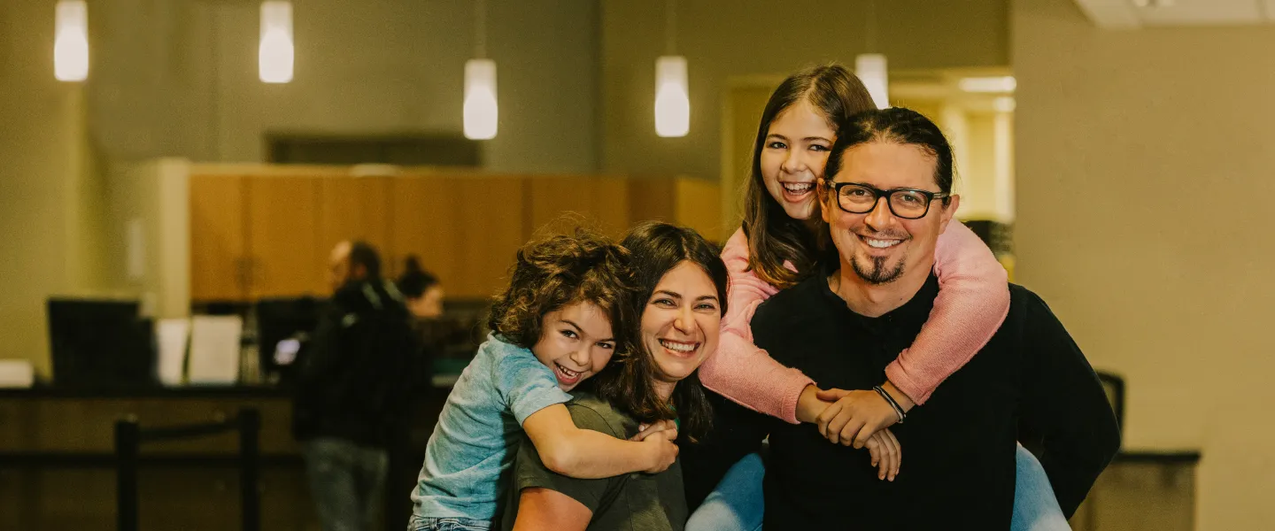 Two young girls latch onto the back of their mother and father in the lobby of a YMCA.