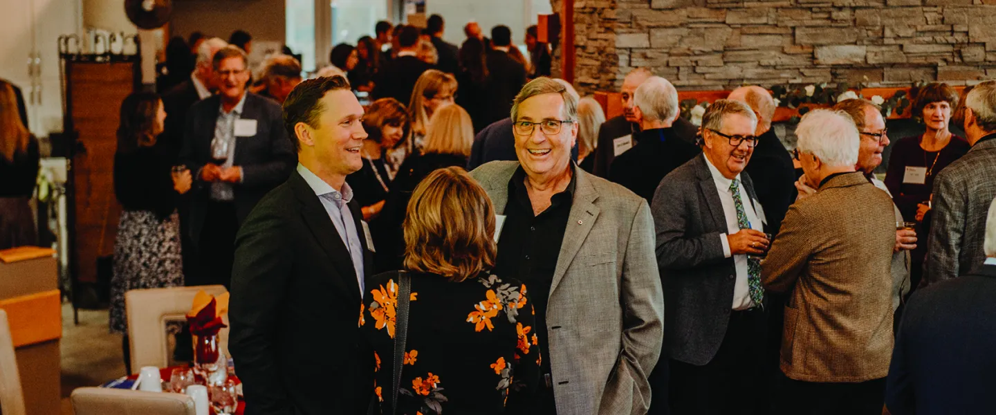 An older man in a suit shares a laugh in a diverse room of people while at a fundraising event.