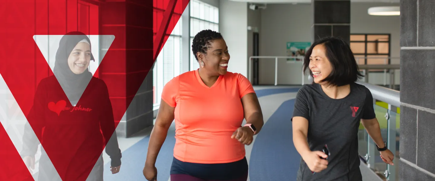 three ladies are walking and passing a smile at each other while walking on an indoor walking track at the Y