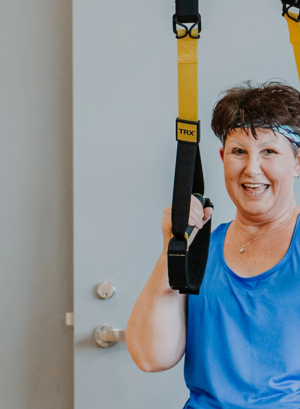 An older women wearing athleisure clothing uses TRX bands during a workout in a fitness studio.