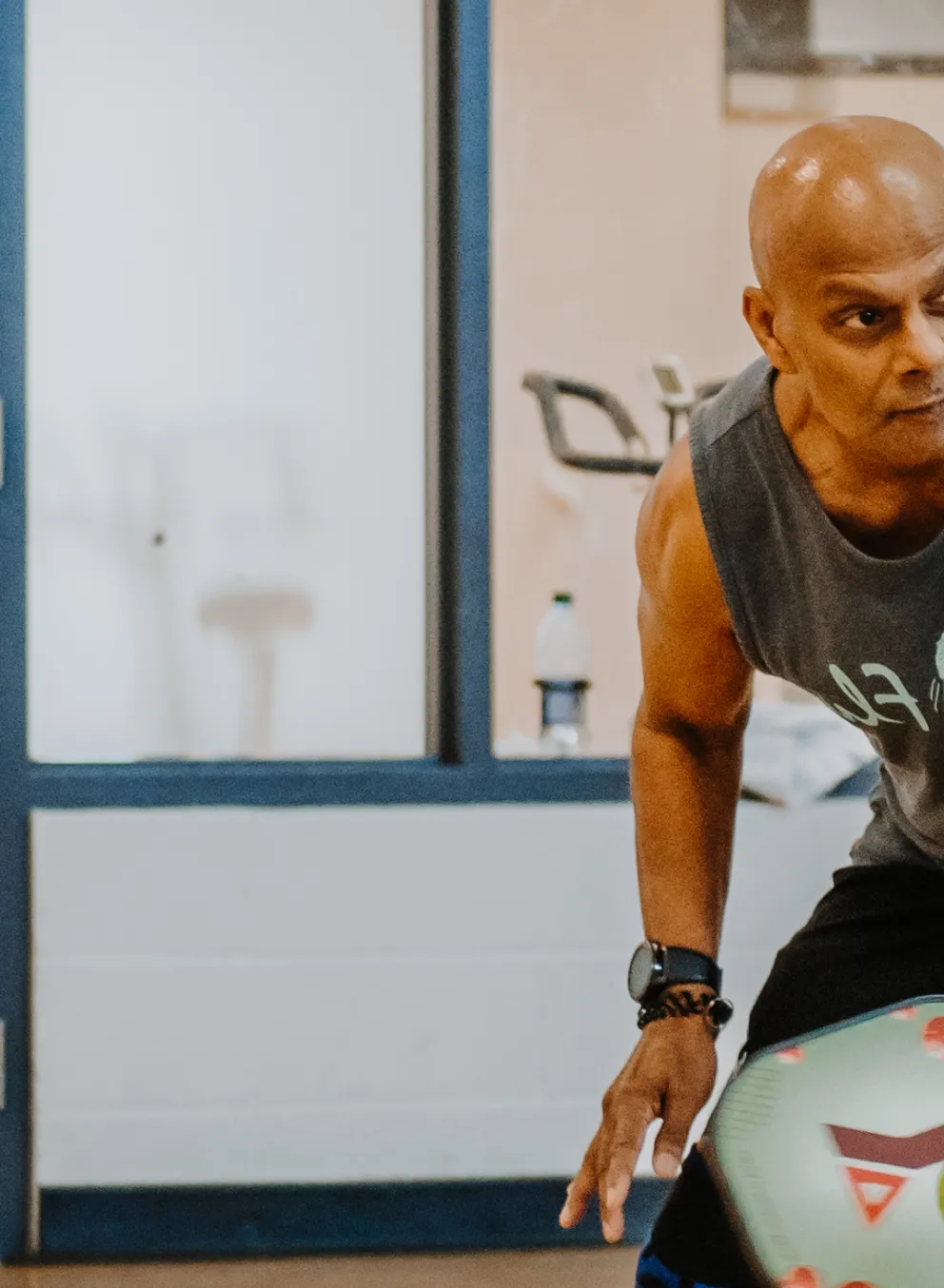 A man winds up for a swing while playing pickleball in a gymnasium.