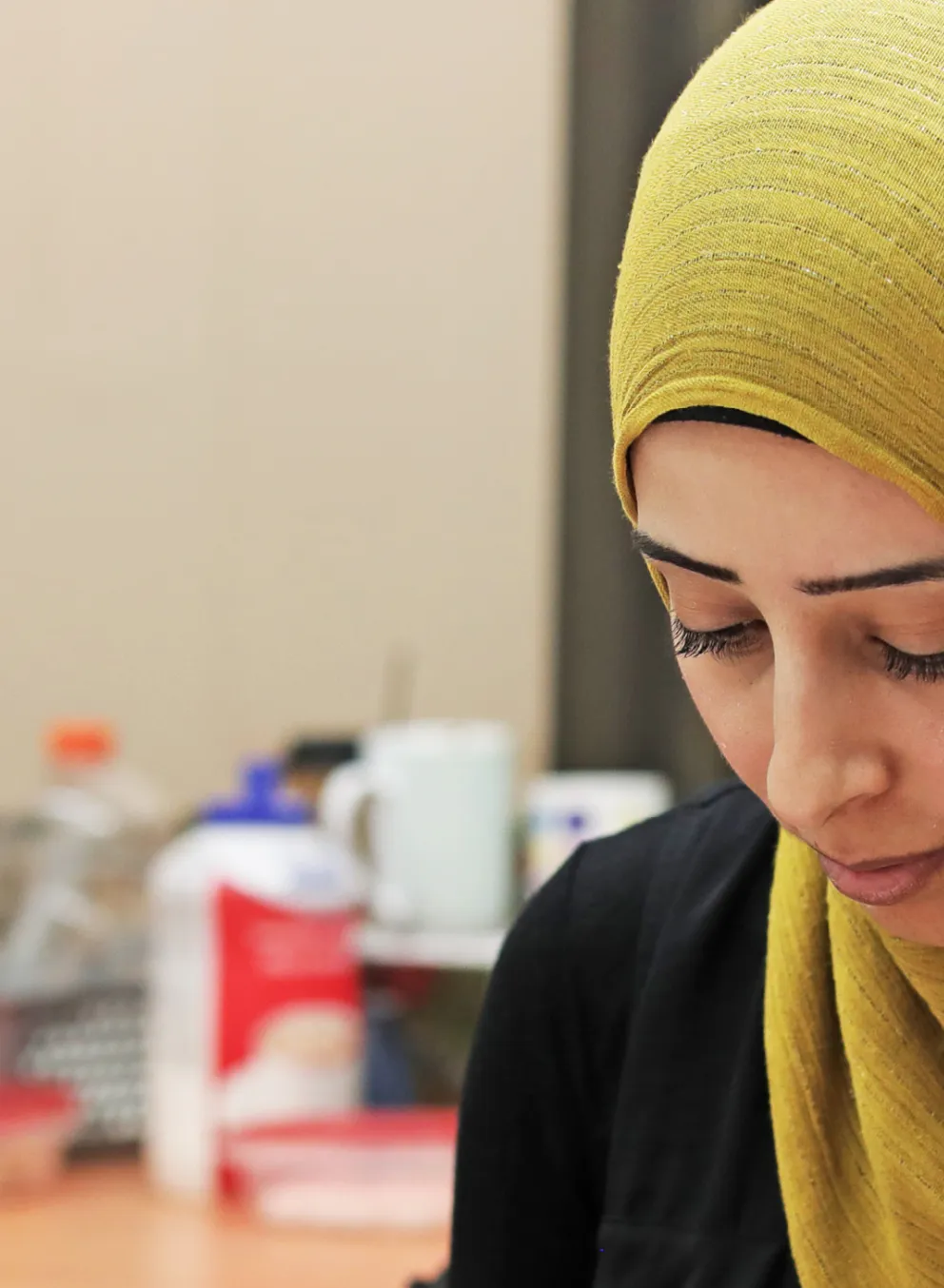 A woman wearing a hijab sits at a table and writes notes during a workshop.