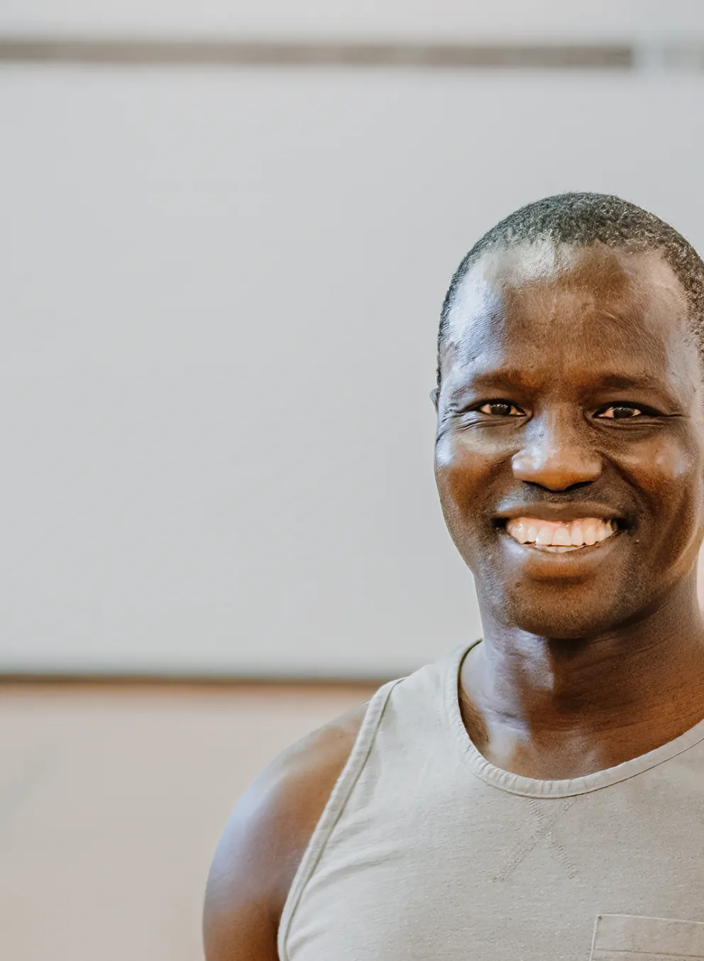 A smiling man stands in a gymnasium with members playing pickleball in the background.
