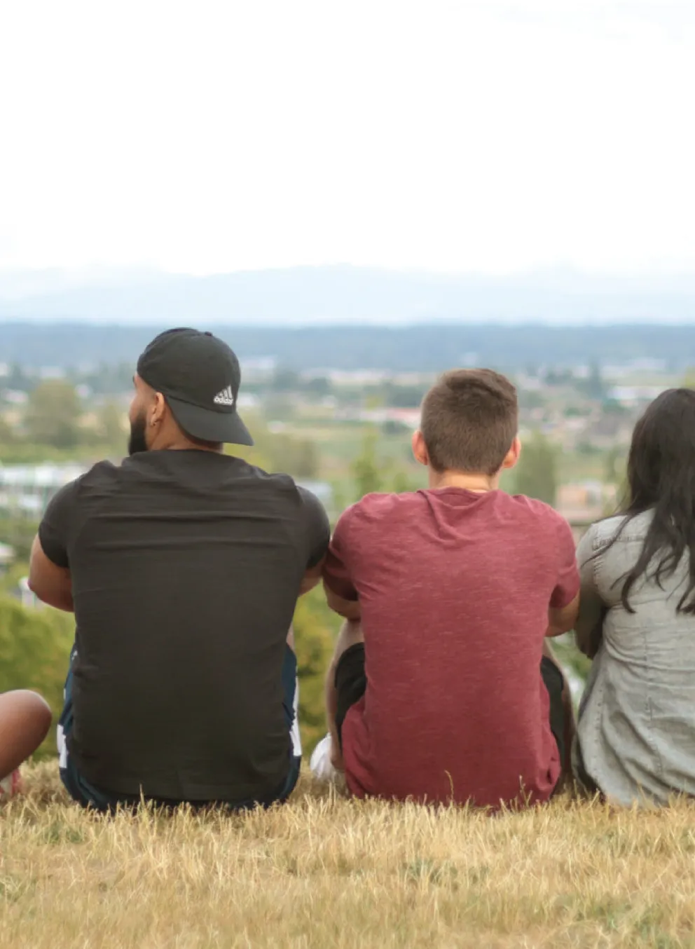 A group of teens and program facilitators sitting on top of a hill, overlooking a city.