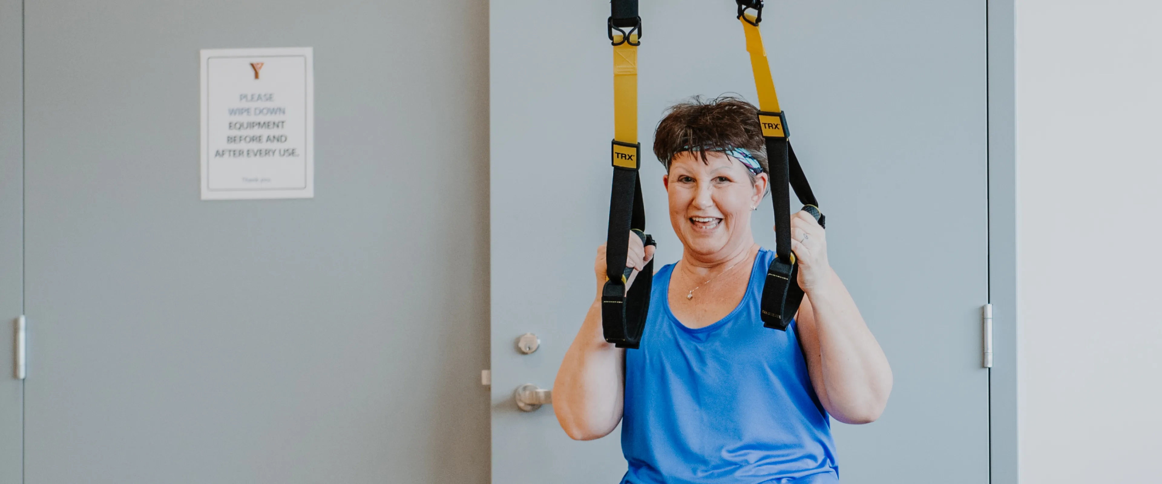 An older women wearing athleisure clothing uses TRX bands during a workout in a fitness studio.
