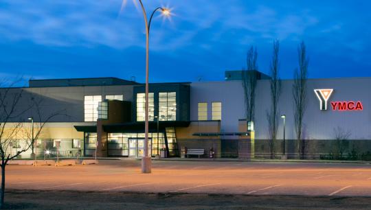 A large building glows in the night sky with interior lights shimering through large windows.