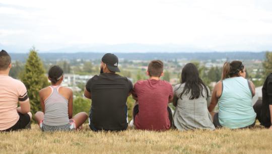 A group of teens and program facilitators sitting on top of a hill, overlooking a city.