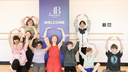 Ballet class posing in front of a banner