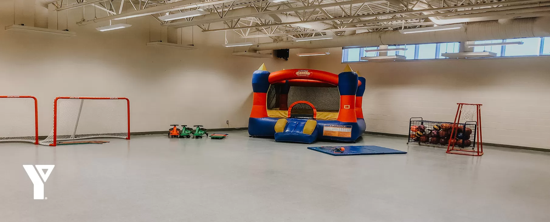 A large multipurpose room seen with hockey nets, basketballs and a medium-sized inflatable bouncy castle.