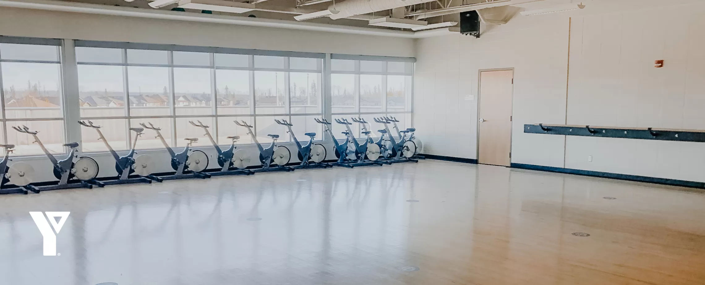 A sun-filled, wood-floored studio space with stationary bikes neatly organized against a wall of windows.