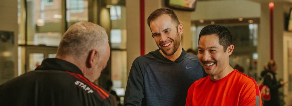 Two men standing at a YMCA front desk, talking to a YMCA staff member.