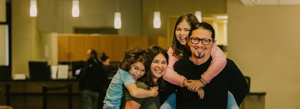 Two young girls latch onto the back of their mother and father in the lobby of a YMCA.