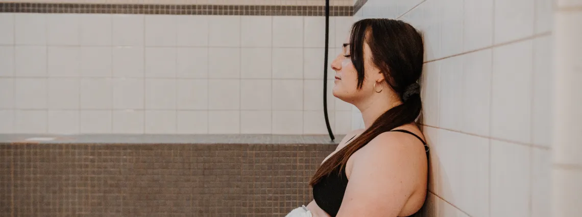 A young woman wears a bathing suit and a towel as she sits in a steamroom.