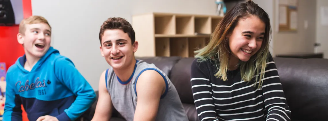 A group of youth sit together on a couch while in a teen lounge.