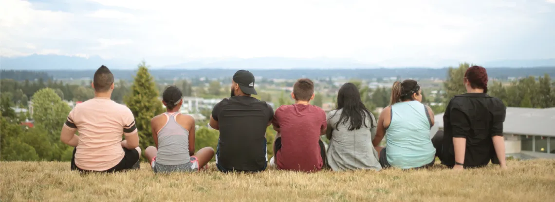 A group of teens and program facilitators sitting on top of a hill, overlooking a city.